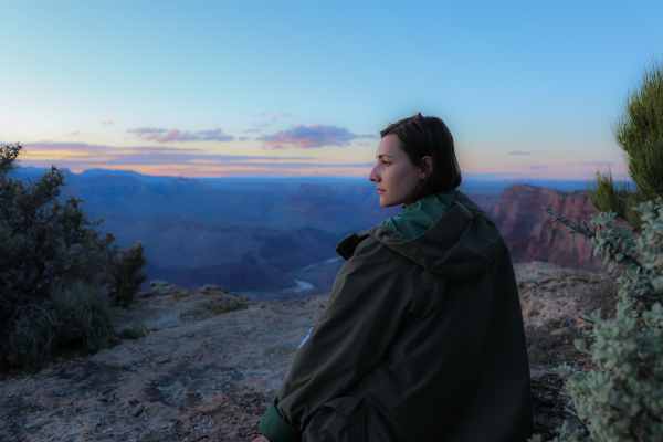 Mulher reflexiva em pé em frente a uma montanha, olhando para os montes. Ela parece estar lidando com o fim de um relacionamento após traição.