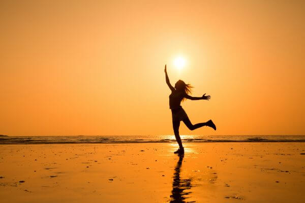 Tem uma moça na praia, com o pé direito no chão e o braço direito esticado para o alto. Vê-se apenas sua silhueta. O sol aparece um pouco acima de sua cabeça e toda a foto tem uma cor alaranjada. O contraste de seu braço esticado e apontado para o alto, com seu pé no chão, nos reporta ao contraste entre a vida e a morte.