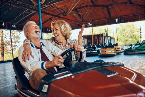 Um casal, uma senhora e um senhor em um carrinho movido a eletricidade de um play center, Daqueles carrinhos que têm borracha em volta, para amortecer as batidas que podem dar uns nos outros. O a mulher está bem sorridente, como quem conta uma piada. E o homem, está dando uma gargalhada. Esta imagem ilustra que o medo da morte não existe para quem vive com plenitude